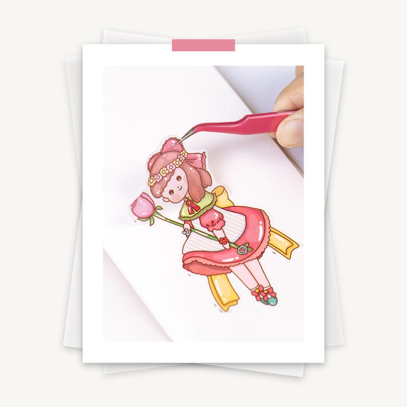 May include: A colorful sticker of a cartoon girl in a pink dress holding a pink flower. The sticker is being held by pink tweezers. The girl has brown hair and a pink bow. The sticker is on a white background.