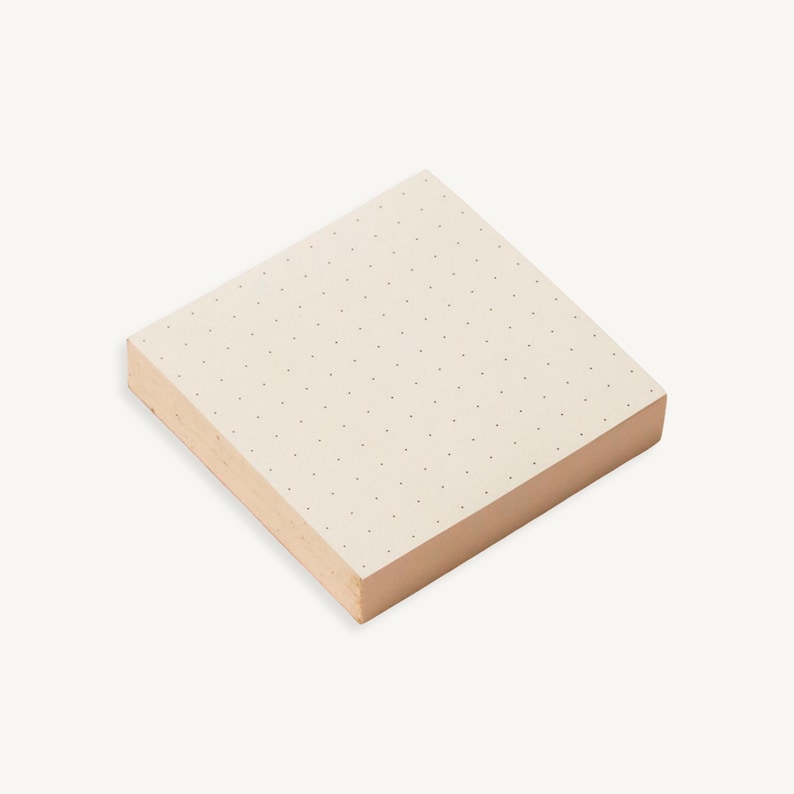May include: A stack of white sticky notes with a subtle dotted pattern. The notes are square shaped and have a slightly textured surface.