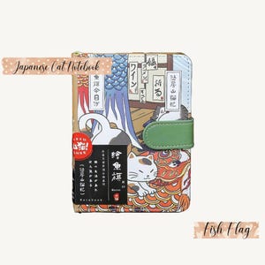 May include: A Japanese-style notebook with a colorful cover featuring cats, fish, and Japanese text. The cover has a green strap closure and the text "Japanese Cat Notebook" is printed on a pink and white polka dot sticker.