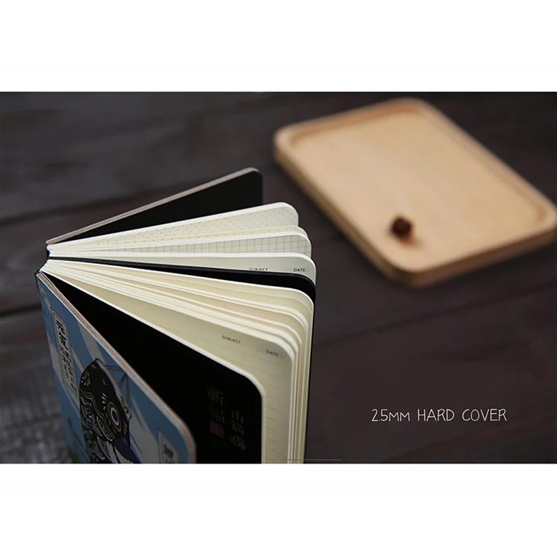 May include: A black hard cover notebook with a colorful illustration of a fish on the front. The notebook is open to reveal different types of paper, including lined, grid, and blank. The notebook is 25mm thick.