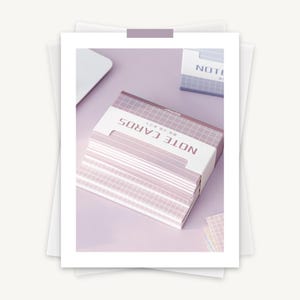 May include: A stack of pink note cards with a grid pattern. The cards are packaged in a pink box with the text "NOTE CARDS" and "罫線入りメモ" in white.