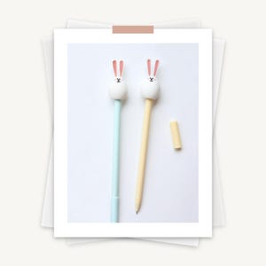 Puede incluir: Dos bol&iacute;grafos con tapas de conejito. Un bol&iacute;grafo es azul claro y el otro es amarillo.