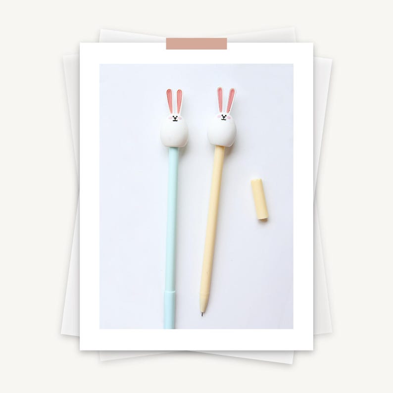 Puede incluir: Dos bol&iacute;grafos con tapas de conejito. Un bol&iacute;grafo es azul claro y el otro es amarillo.