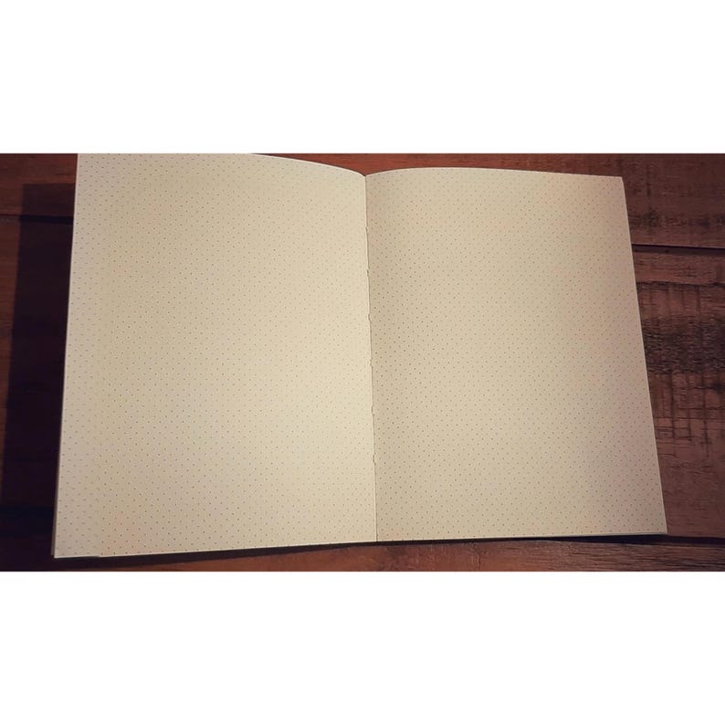 May include: An open notebook with a dotted grid pattern on the pages. The notebook has a brown cover and is lying open on a wooden surface.