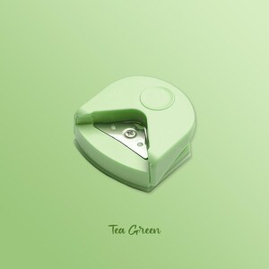K&ouml;nnte beinhalten: Ein gr&uuml;nes Eckrundungswerkzeug mit einer Metallschneide. Das Werkzeug ist zum Abrunden der Ecken von Papier gedacht. Das Werkzeug ist mit "Tea Green" beschriftet.