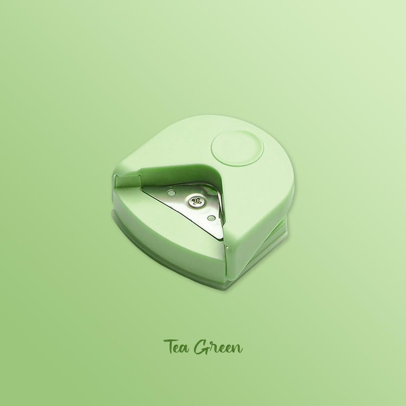 K&ouml;nnte beinhalten: Ein gr&uuml;nes Eckrundungswerkzeug mit einer Metallschneide. Das Werkzeug ist zum Abrunden der Ecken von Papier gedacht. Das Werkzeug ist mit "Tea Green" beschriftet.