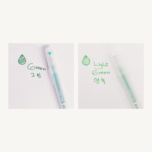 May include: Two clear plastic pens with green ink. The pen on the left has a light blue ink color and the pen on the right has a light green ink color. The pens are labeled "Green" and "Light Green" in English and Korean.