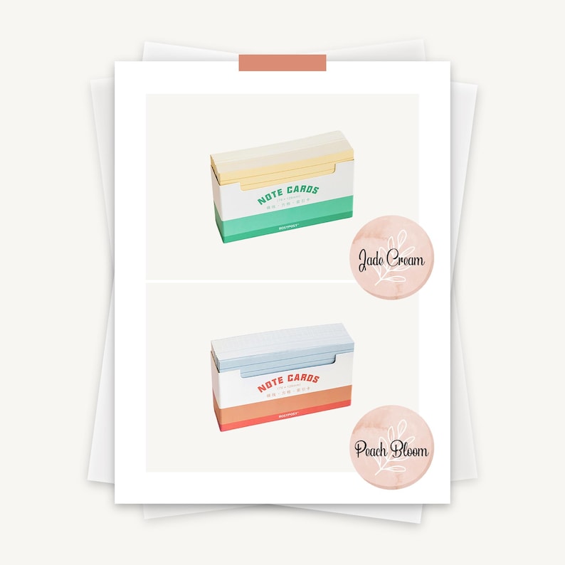 May include: Two boxes of note cards, one with a yellow and white design and the text "NOTE CARDS" and the other with a blue and white design and the text "NOTE CARDS". The boxes are on a white background with a pink circle with the text "Peach Bloom" and a green circle with the text "Jade Cream".