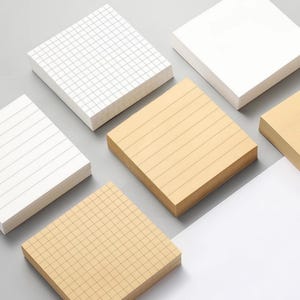 May include: Five stacks of square sticky notes in different patterns. Two stacks are white with black lines, one is white with a grid pattern, and two are beige with black lines. The stacks are arranged in a staggered pattern on a gray surface.