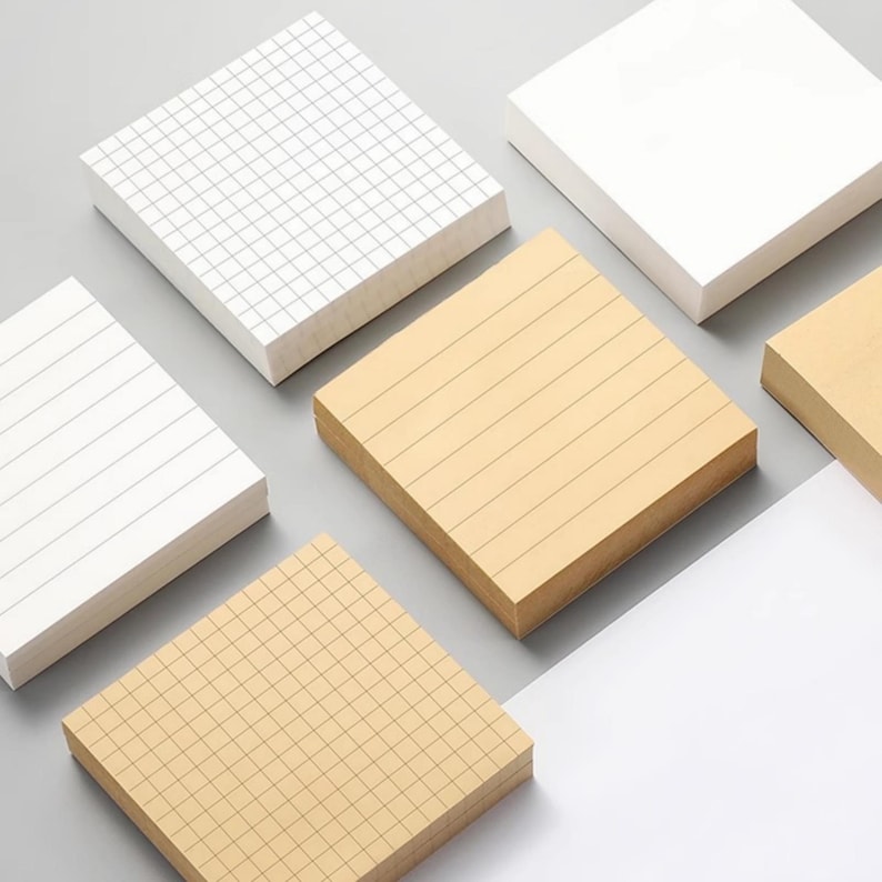 May include: Five stacks of square sticky notes in different patterns. Two stacks are white with black lines, one is white with a grid pattern, and two are beige with black lines. The stacks are arranged in a staggered pattern on a gray surface.