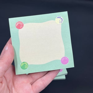 May include: A stack of green sticky notes with a white center and colorful circles in each corner. The circles have a yellow, red, green, and purple design.