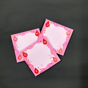 May include: Three pink square sticky notes with a white center and red blood drop icons with the letters A, B, AB, and O printed on them.