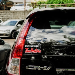 May include: A black car with a Tim Hortons sticker on the back window. The sticker says "Arrêts fréquents au Tim Hortons" and features a white coffee cup.