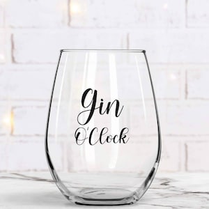 May include: A clear glass wine glass with the text "Gin O'Clock" printed on it.