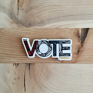 May include: A white sticker with the word "VOTE" in black, red, and gray stylized lettering. The text "Your" appears above the word "VOTE" and the text "Matters." appears below the word "VOTE".