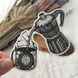 May include: Black and white line art sticker of a coffee pot pouring coffee into a mug. The mug has the word "COFFEE" written on it.