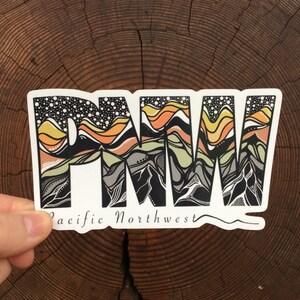 Puede incluir: Una pegatina blanca con una ilustraci&oacute;n en blanco y negro de monta&ntilde;as y el texto "PNW" en una fuente estilizada. El texto "Pacific Northwest" est&aacute; escrito debajo de la ilustraci&oacute;n.