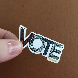 May include: A sticker with the word "VOTE" in black and white with red, blue, and white accents. The word "Your" is above the word "VOTE" and the word "Matters." is below the word "VOTE".