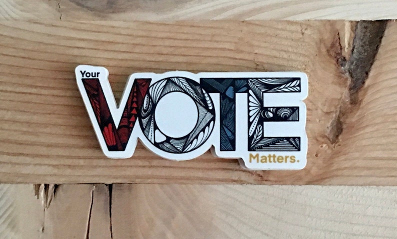 May include: A white sticker with the word "VOTE" in black outlined letters. Each letter is filled with a different patterned design. The "V" is red and white, the "O" is black and white, the "T" is blue and white, and the "E" is black and white. The sticker also says "Your" above the word "VOTE" and "Matters." below the word "VOTE".