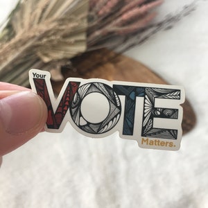May include: A sticker with the word "VOTE" in stylized lettering. The letters are outlined in black and filled with red, white, and blue. The text "Your" appears above the word "VOTE" and the text "Matters." appears below the word "VOTE".