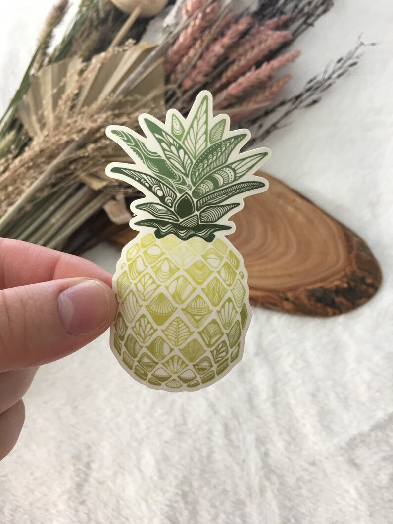 May include: A green and yellow pineapple sticker with a detailed, intricate design. The pineapple is drawn with a pattern of leaves and scales.