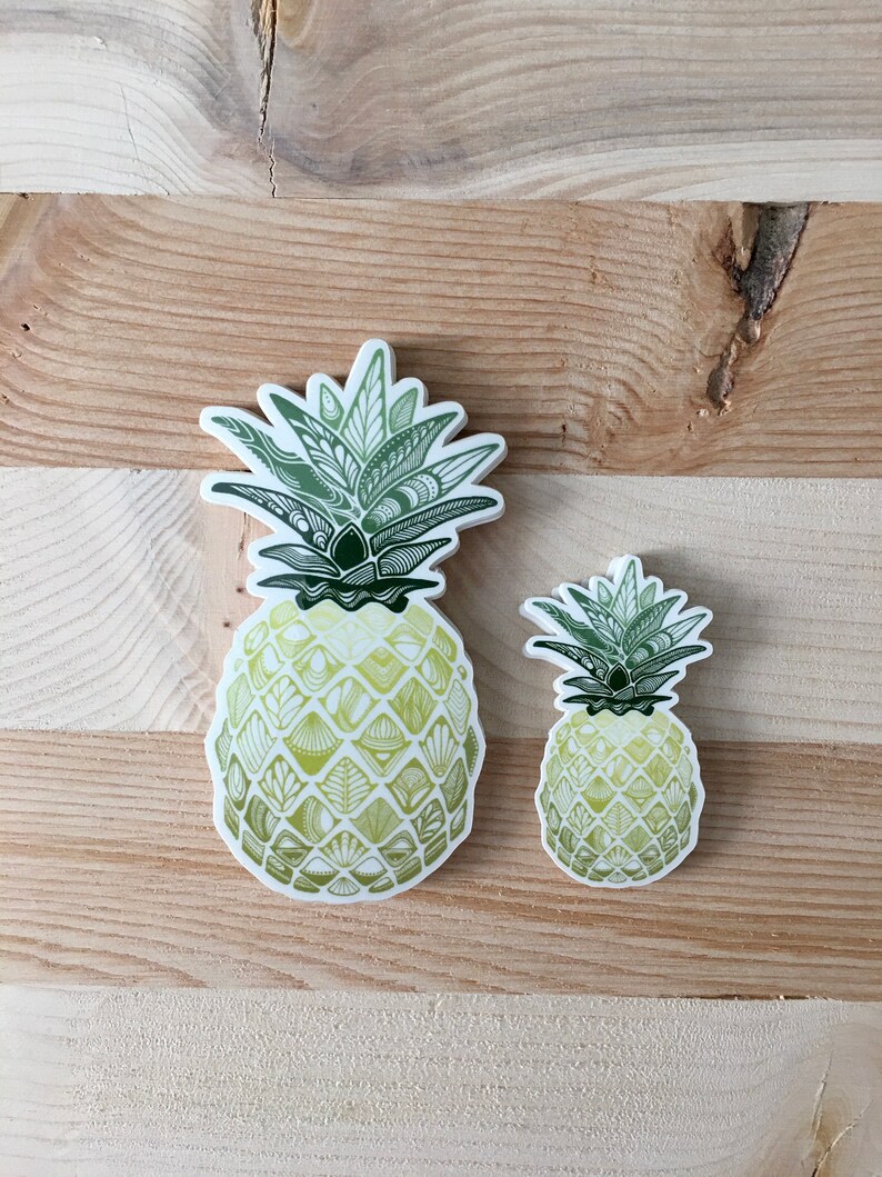 May include: Two pineapple stickers with a green and yellow patterned design. The larger sticker is on the left and the smaller sticker is on the right.