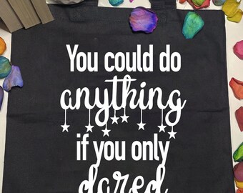 Peut inclure: Sac fourre-tout noir avec du texte blanc qui dit "You could do anything if you only dared" avec des étoiles suspendues aux lettres.