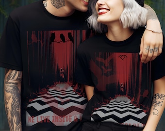 May include: A couple wearing black t-shirts with a red and black graphic print of a forest path with a black and white chevron pattern at the bottom. The text "WE LIVE INSIDE A" is printed on the bottom of the shirt. The graphic also includes three black birds perched on a branch.