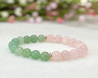 May include: A beaded bracelet featuring a gradient of green and pink gemstones. The bracelet transitions from green beads to pink beads, with gold-colored spacers. The bracelet is displayed on a white surface.