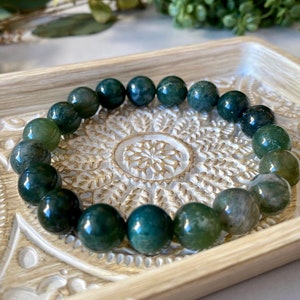 May include: A green agate gemstone bracelet with round beads. The bracelet is displayed on a decorative wooden tray.