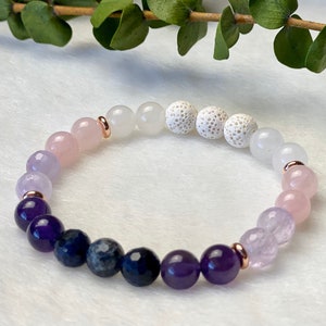 May include: A multi-coloured gemstone bracelet with lavender, pink, purple and blue beads. The bracelet has rose gold accents and white lava beads.
