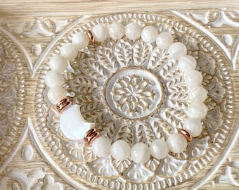 May include: White moonstone beaded bracelet with rose gold accents. The bracelet is made with round beads and a crescent moon charm.