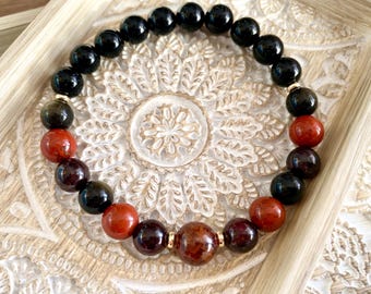 May include: A bracelet made of black, red, and brown beads. The bracelet has a gold accent.