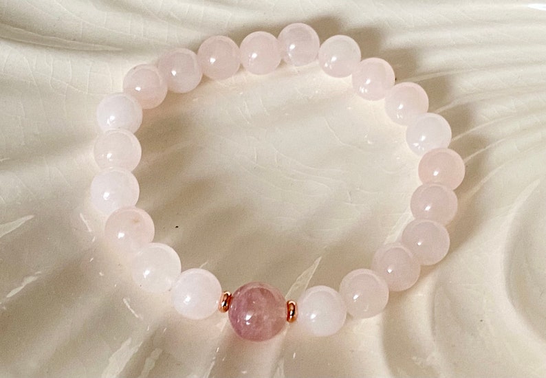 Pu&ograve; includere: Un braccialetto di pietre bianche con un unico ciondolo rosa al centro. Il braccialetto &egrave; realizzato con dettagli in oro rosa.