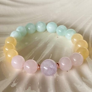 May include: A pastel-colored gemstone bracelet with yellow, green, and pink beads. The bracelet has a single lavender bead in the center.