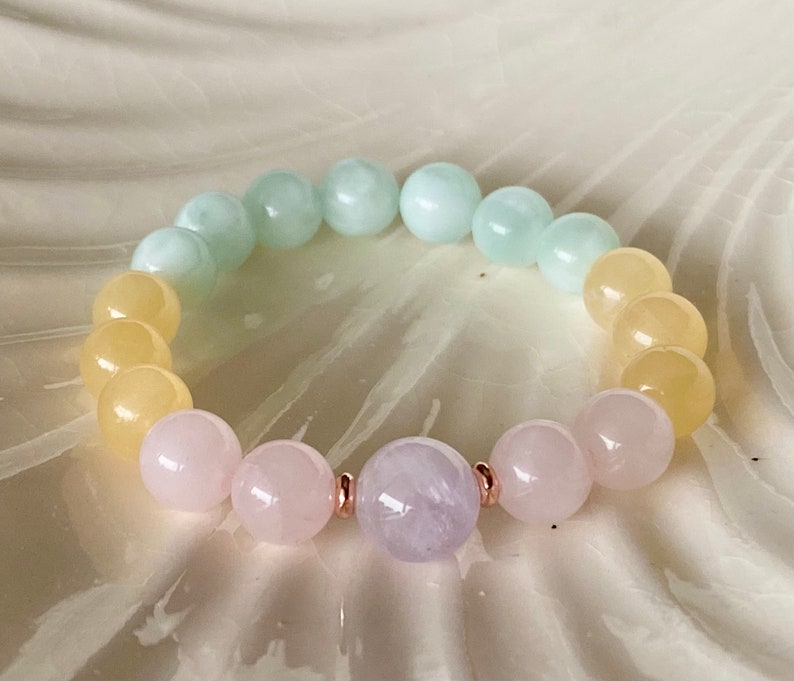 May include: A pastel-colored gemstone bracelet with yellow, green, and pink beads. The bracelet has a single lavender bead in the center.