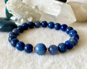 May include: A blue gemstone bracelet with a single larger bead in the center. The bracelet is made with round beads and has a rose gold accent.