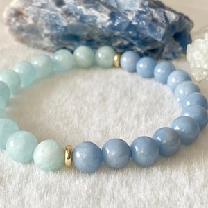 May include: A light blue and aqua blue gemstone bracelet with gold spacers. The bracelet is made of round beads and is approximately 7 inches in length.