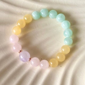May include: A pastel-colored beaded bracelet with light pink, yellow, and light green beads. The bracelet has a single lavender bead with rose gold accents.