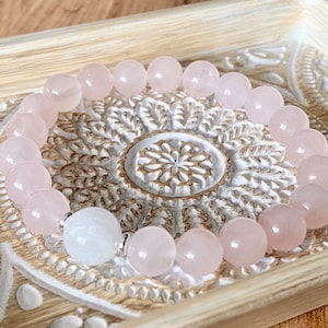 May include: A pink rose quartz bracelet with a white moonstone bead. The bracelet is made of smooth, round beads and is strung on elastic.