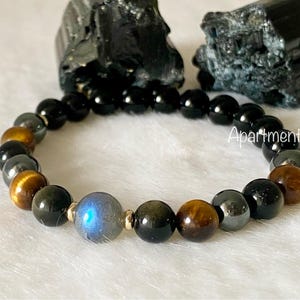 May include: A black, brown and gold beaded bracelet with a blue labradorite gemstone bead. The bracelet is made with tiger's eye, black onyx and hematite beads.