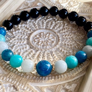 May include: A bracelet made of black, white and blue beads. The bracelet is made of natural stones and is strung on a gold chain.