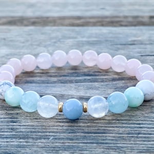 May include: A bracelet made with pink, light blue and white beads. The bracelet has gold accents.