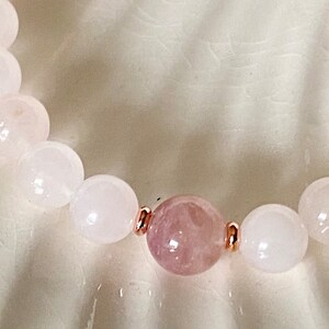 Pu&ograve; includere: Un braccialetto di perline rosa e bianche con accenti in oro rosa. Il braccialetto presenta un perno rosa pi&ugrave; grande al centro.
