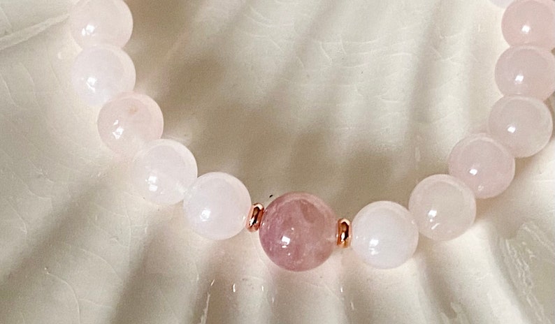 Pu&ograve; includere: Un braccialetto di perline rosa e bianche con accenti in oro rosa. Il braccialetto presenta un perno rosa pi&ugrave; grande al centro.