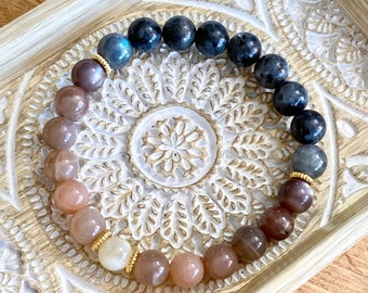 May include: A beaded bracelet with a gradient of colors, starting with light brown and transitioning to dark gray. The bracelet is made with round beads and has gold accents.