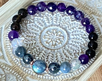 May include: A bracelet made with amethyst, labradorite, smoky quartz, and clear quartz beads. The beads are strung on a stretchy cord and have a copper accent.