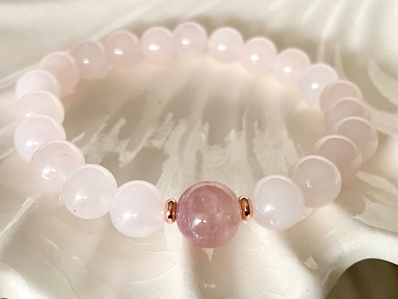 Pu&ograve; includere: Un braccialetto di perline rosa e bianche con una perla rosa pi&ugrave; grande al centro. Il braccialetto &egrave; fatto di pietre naturali e ha un accento oro rosa.