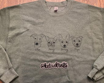 May include: Green sweatshirt featuring four dog portraits with names Olive, Henry, Harvey, and Piper. The sweatshirt has a crew neck and long sleeves. The text "@kelciekrafts" is embroidered at the bottom.