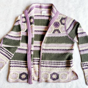 Könnte beinhalten: Handgefertigte Häkeljacke in Olivgrün, Lavendel und Creme. Die Jacke hat einen Reißverschluss vorne, lange Ärmel und geometrische Muster. Das Häkeldesign umfasst sechseckige und florale Motive.